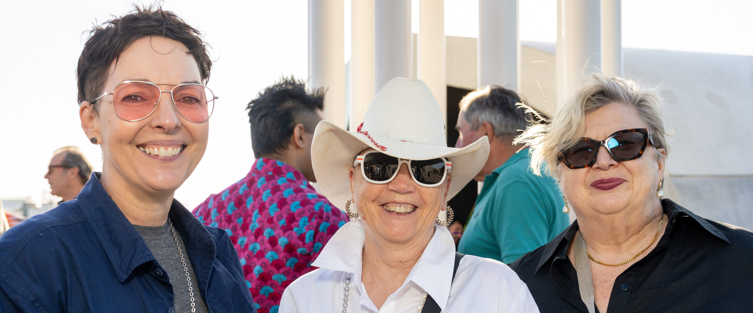 Three people smiling at the camera, middle person wearing a hat