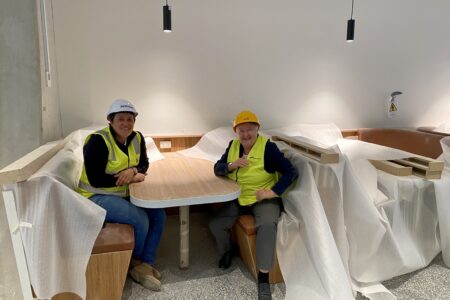 Photo of Jude Munro and Jemma Bates on the building site, sitting at a booth.