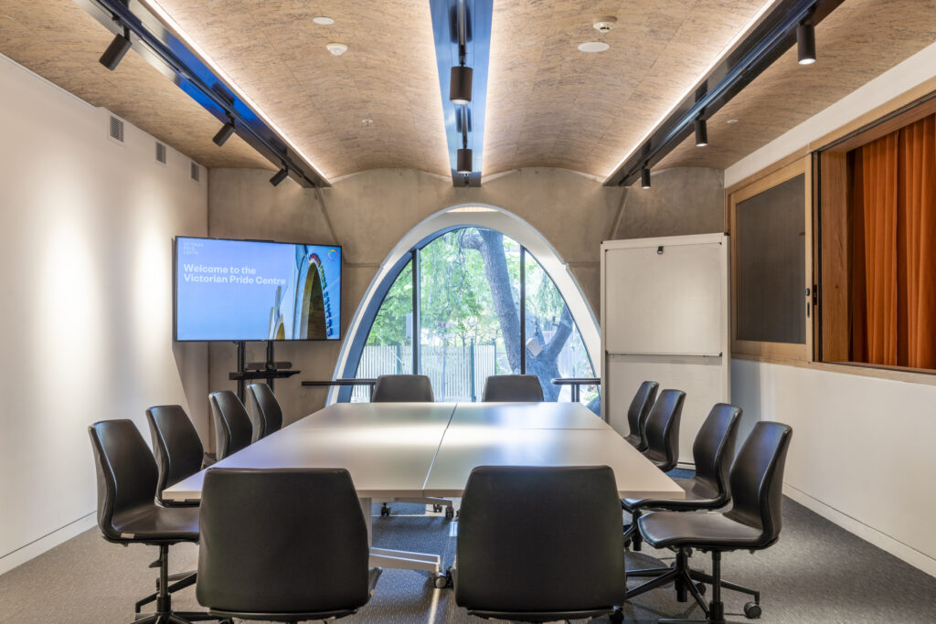 Mezzanine Room; table and chairs in the middle with a white board, tv and window pictured behind. A window to the Theatrette to the right.