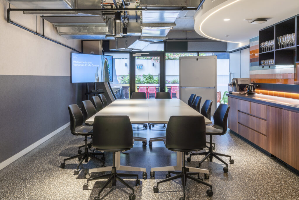 Table with chairs, a kitchenette to the right, TV and whiteboard.