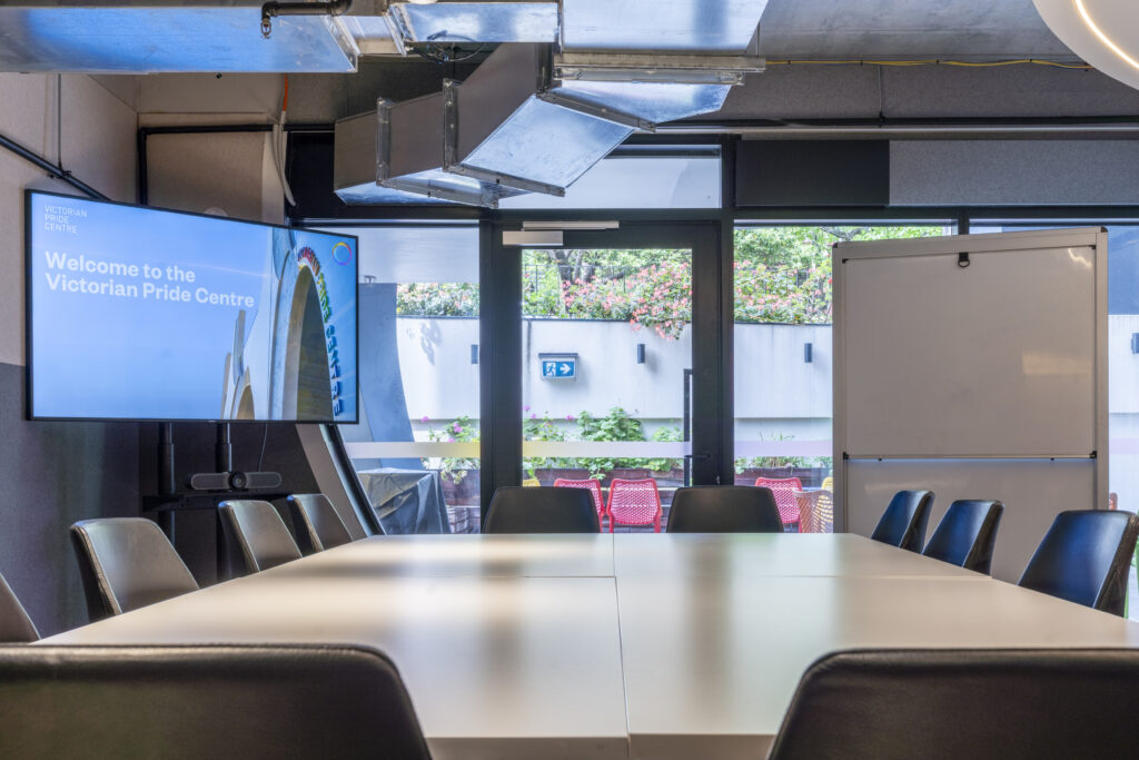 Boardroom; medium shot of table with chairs in the centre of the room, TV and whiteboard. Courtyard is behind.