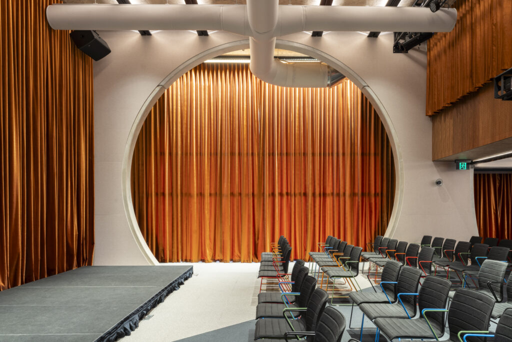 Theatrette, chairs, stage, large orange velvet curtains, circle framing against the curtains