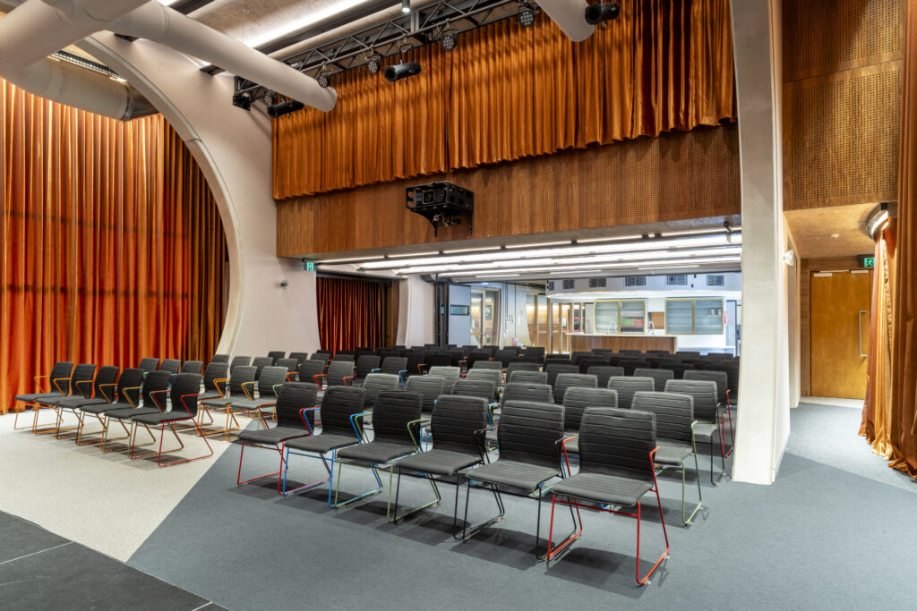 Captured from the stage, bars and various chairs in a row with bar captured behind. Mezzanine curtains/window above.