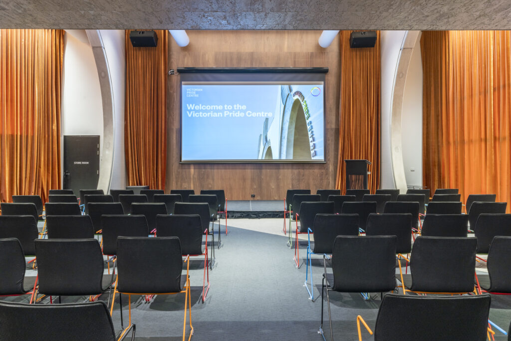 Theatrette with chairs in various rows, a screen, bollards and large orange and velvet curtains