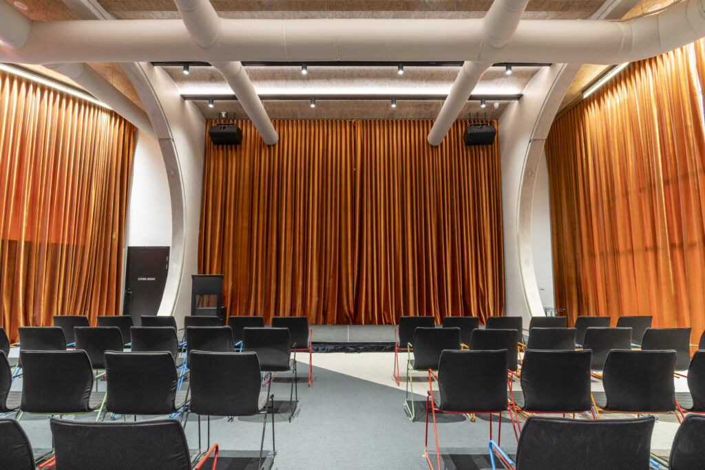 Theatrette, rows of chairs facing the stage and large velvet orange curtains