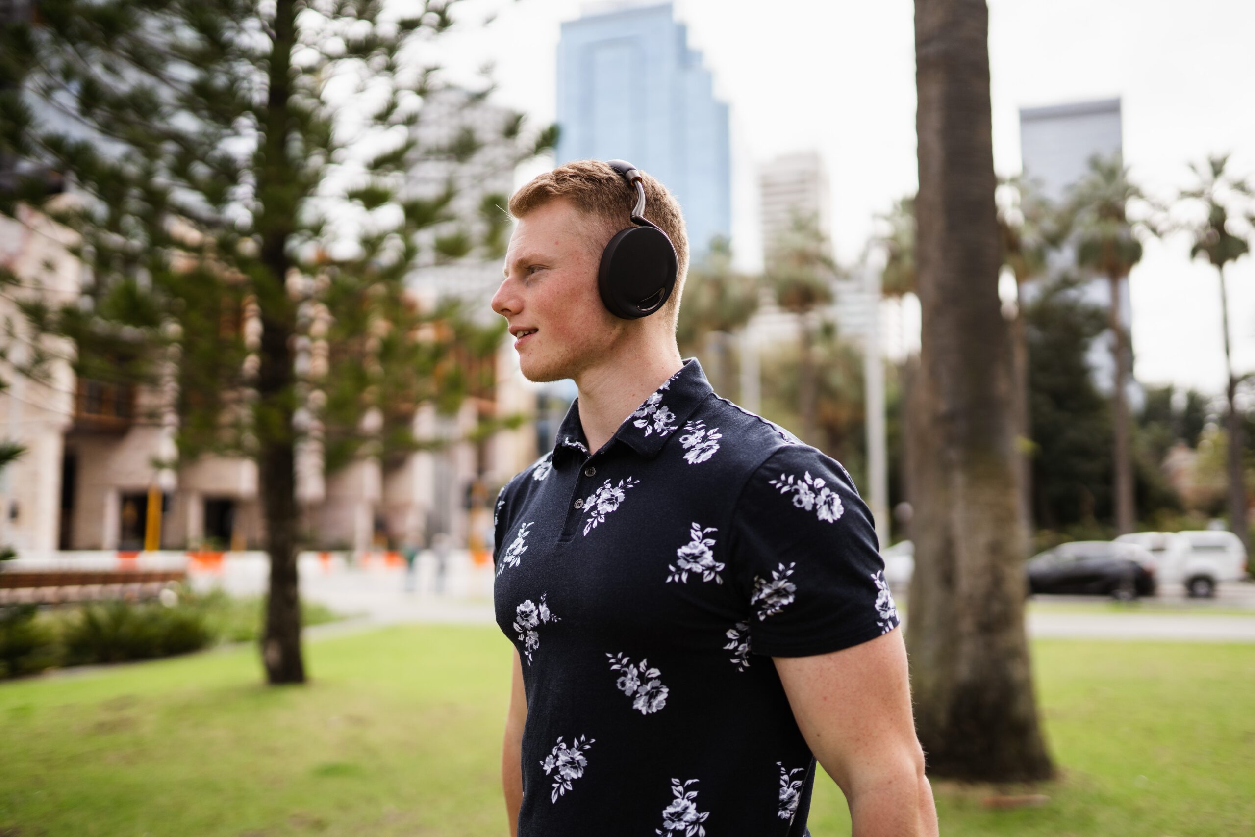 A man in his 20s, smiling, walks through Melbourne wearing large headphones