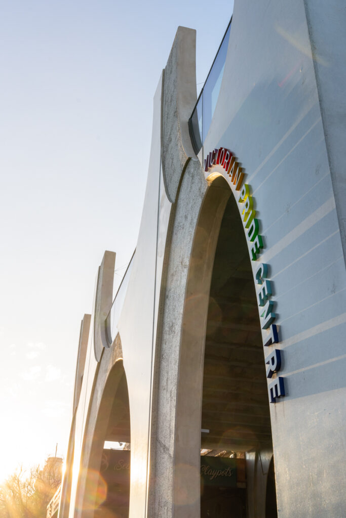 Rainbow letters spelling out Victorian Pride Centre, curved around arch on front of building