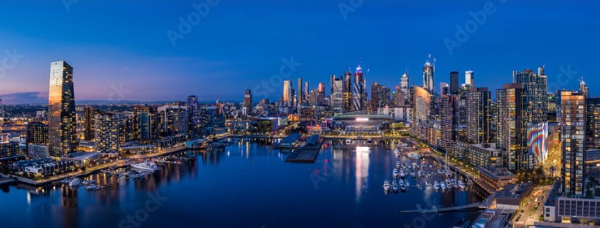 A long shot captured over the water of Docklands at night with the city in the background