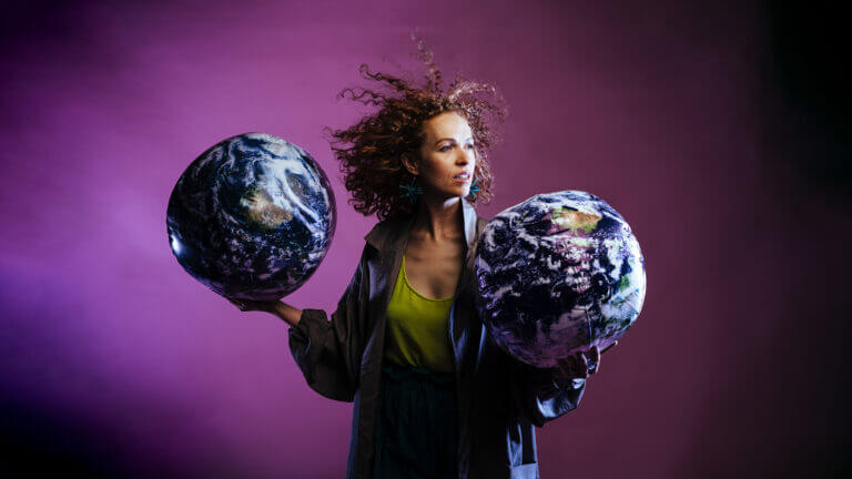 A person looks off to the distance and holds two makeshift blow -up earth sculptures.