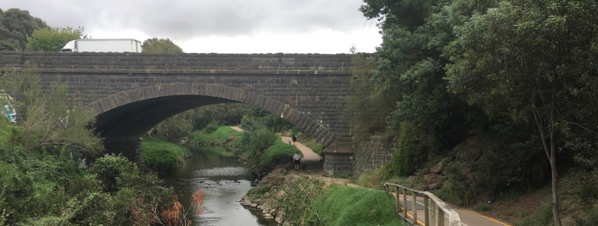 Merri Creek featuring a bridge over the creek with a walking track beside it, where a few people are strolling.