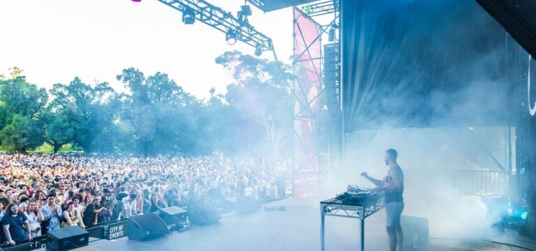 Midsumma Carnival main stage. A DJ performs on stage with a large crowd dancing in front of the stage.