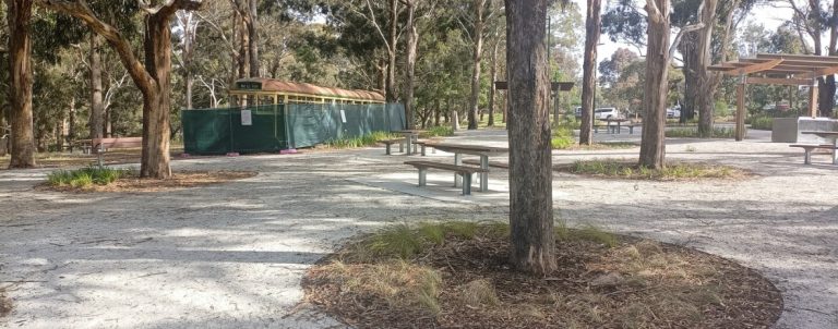 A long shot of a picnic area with trees and an old tram behind a fence.