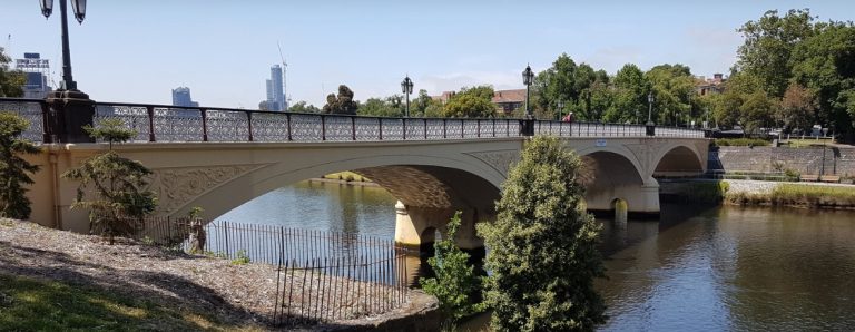 A river with a historical bridge. In the distance, a person looks over the bridge at the river.