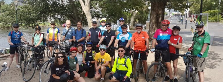 A group of people with bikes and helmets smile at the camera