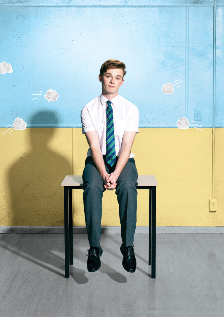 A person in a school uniform sits atop a table, with animated flying pieces of scrunched paper swirling around their head.