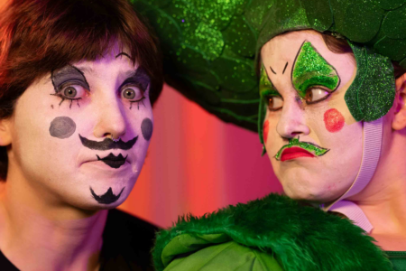 Two people in costumes and clown/drag makeup. They both have large expressions on their face.