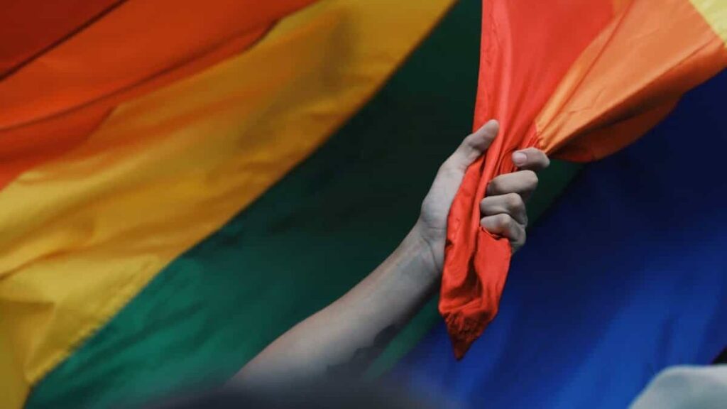 A hand with a tattoo reaching towards and grabbing the Pride Flag