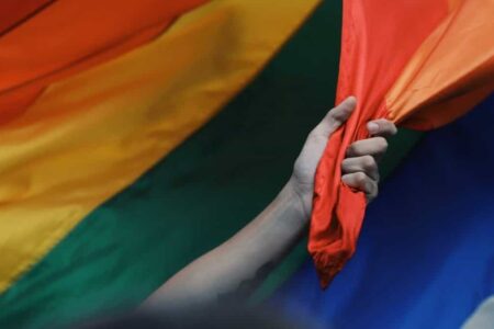 A hand and arm reaches out and grabs the rainbow flag.