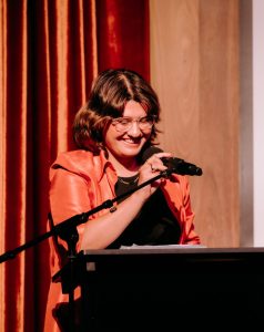 Amber Ryder Headshot - speaking behind a podium on stage in the VPC Theatrette
