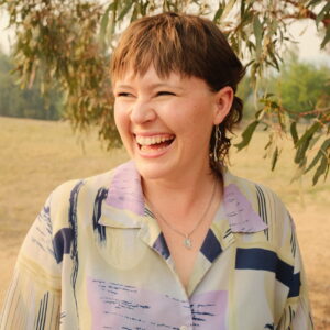 Lauren Swain Headshot with a big smile and a field and eucalypt trees behind